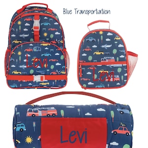 Può includere: Un set composto da zaino, borsa per il pranzo e tappetino per il riposo blu navy con un motivo colorato di trasporti, tra cui auto, camion e aerei. Ogni articolo è personalizzato con il nome Levi in testo rosso o blu e ha finiture rosse.