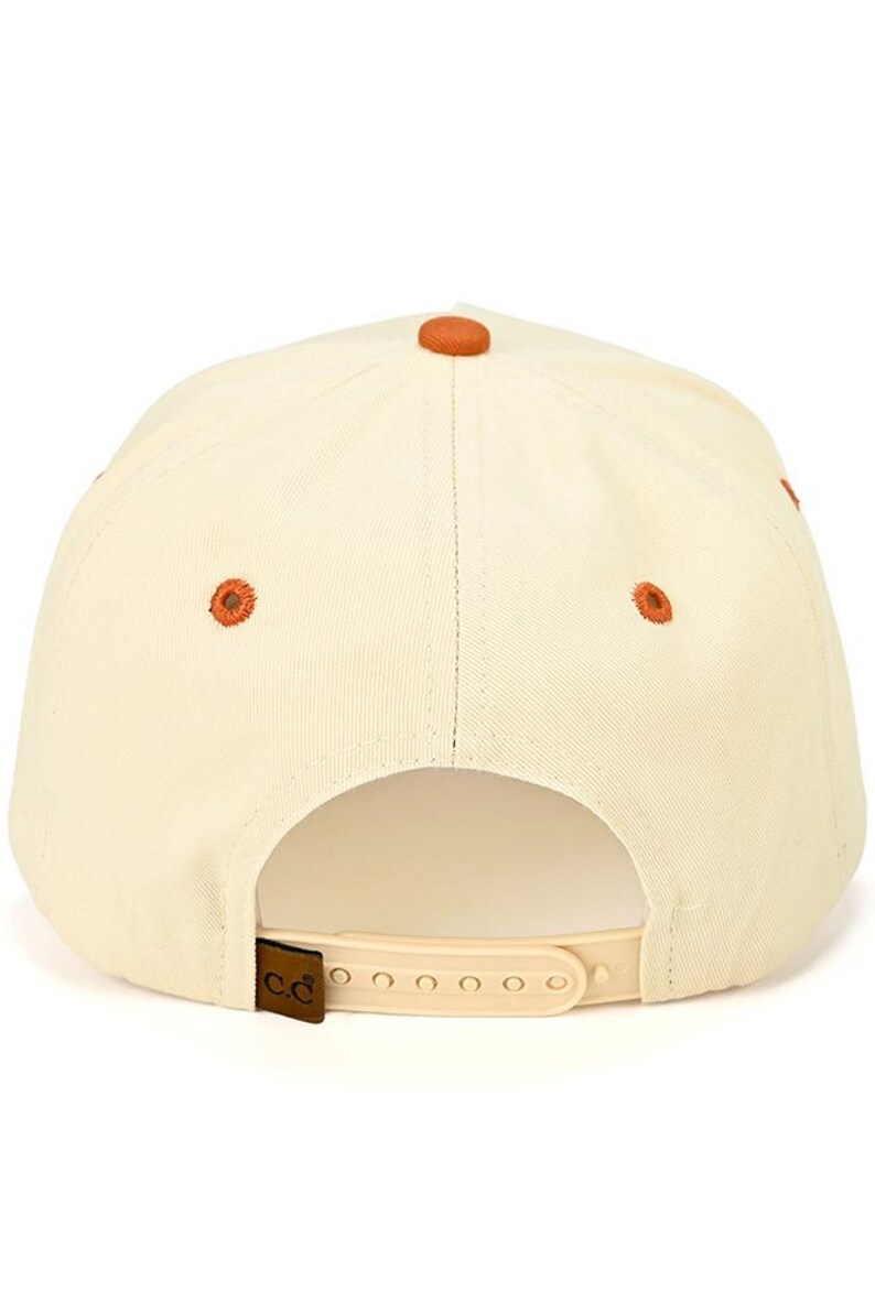 Op de afbeelding: Cr&egrave;mekleurige baseballpet met een gebogen klep en verstelbare band. De pet heeft een bruine knoop aan de bovenkant en bijpassende bruine geborduurde details. De achterkant van de pet heeft een kleine, bruine leren patch met de letters "C.C."