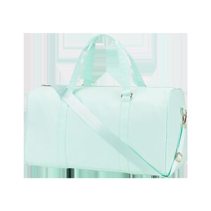 May include: A light blue duffel bag with a long strap and two top handles. The bag has a zipper closure and a gold metal accent.