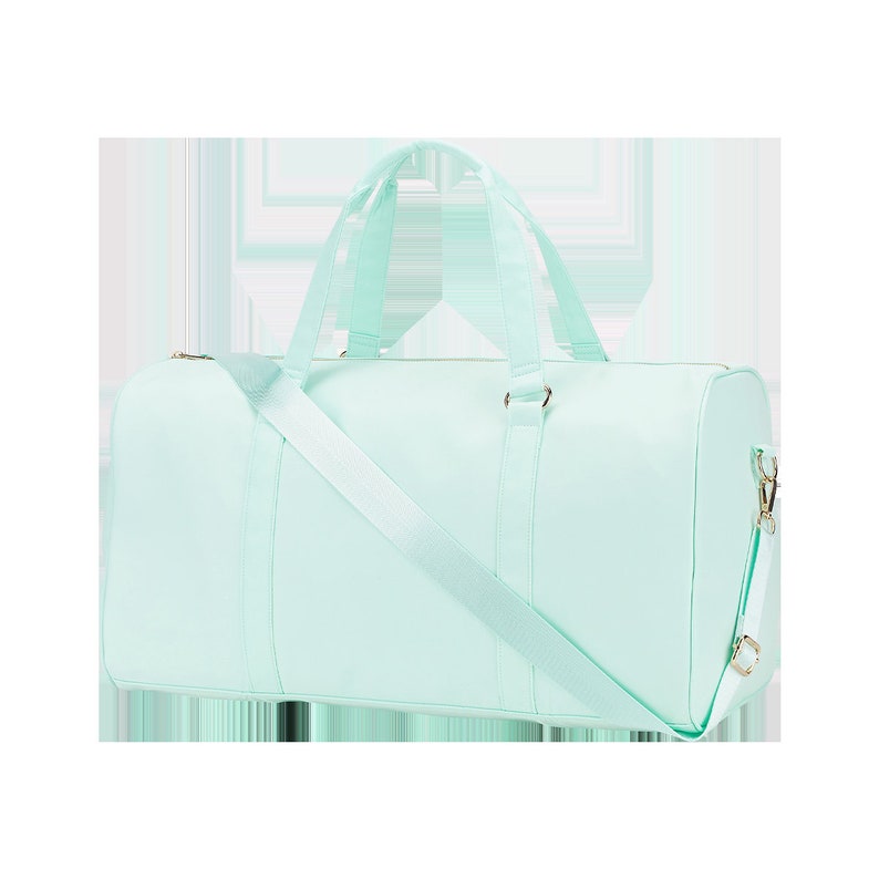 May include: A light blue duffel bag with a long strap and two top handles. The bag has a zipper closure and a gold metal accent.