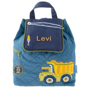 May include: A blue quilted backpack with a yellow dump truck design. The backpack has a flap with a navy blue pocket that says "Levi" in orange lettering. A zipper on the side has a charm that says "Let's Roll" with a gear design.