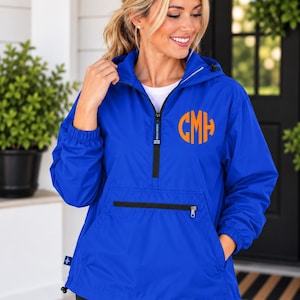 May include: A royal blue pullover windbreaker jacket featuring a hood with adjustable drawstrings, a quarter-zip front closure, and a large front pocket with a black zipper. The jacket displays an orange circular monogram with the letters CMH.