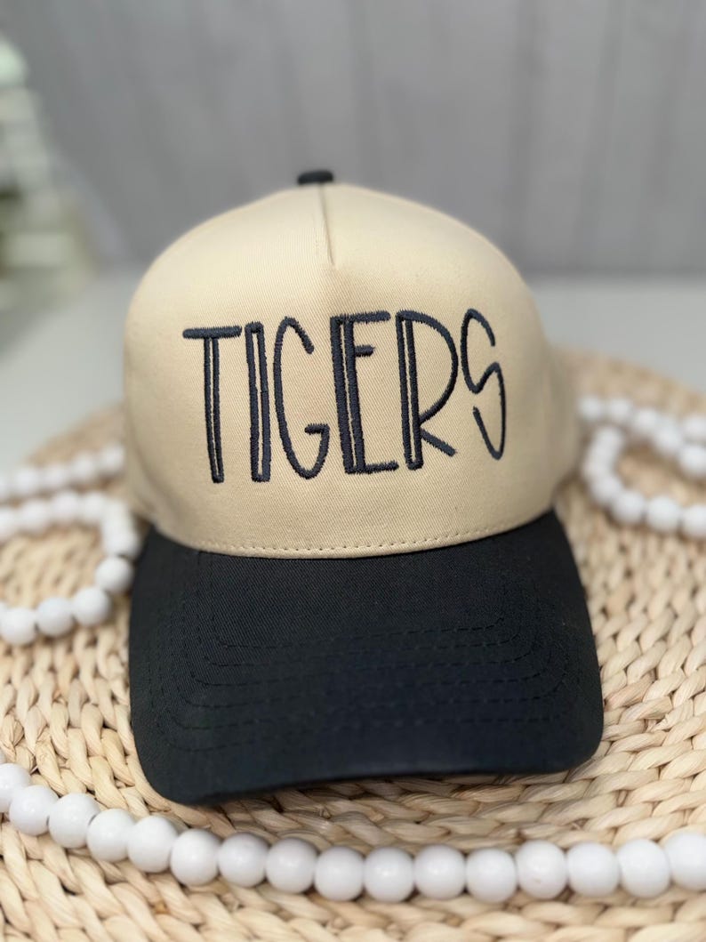 Op de afbeelding: Beige en zwarte baseballcap met het woord "TIGERS" in zwarte letters geborduurd. De cap heeft een gebogen klep en een gestructureerde kroon, geschikt voor vrijetijdskleding. Een modieus accessoire.
