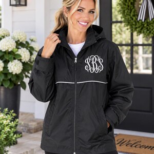 May include: A black hooded windbreaker jacket featuring a full-length front zipper, long sleeves with adjustable cuffs, and a horizontal white piping detail across the chest. The left chest area displays a white embroidered monogram with the letters SBS.
