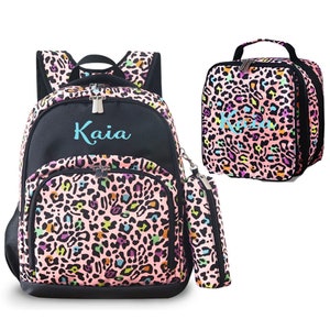May include: A pink and black backpack with a colorful leopard print design. The backpack has a matching lunch bag and pencil case. The name "Kaia" is embroidered on the backpack in blue.