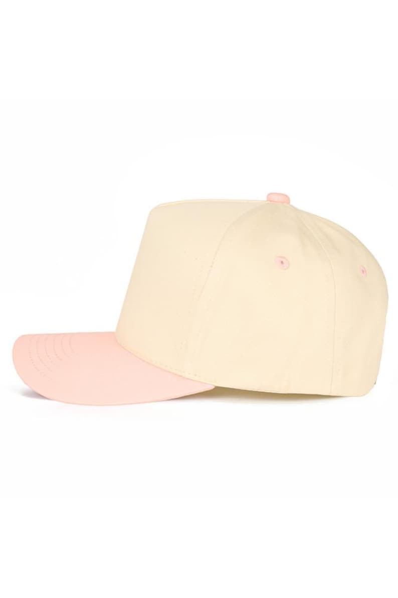 Op de afbeelding: Een baseballcap in cr&egrave;me en roze. De kroon is cr&egrave;me en de klep is roze. De cap heeft een gestructureerd ontwerp met een platte klep en een roze knoop. Een modieus accessoire voor dagelijks gebruik.
