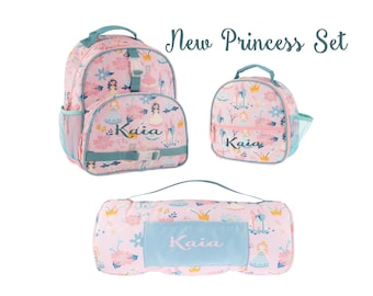 May include: A pink princess-themed set including a backpack, lunch bag, and blanket. The set features a floral pattern with princess illustrations and the name "Kaia". The backpack and lunch bag have teal accents, and the blanket is rolled up.