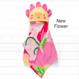 May include: Pink hooded towel with a floral design and a yellow flower-shaped hood with a smiling face. The text "New Flower" is written in black on a white background.
