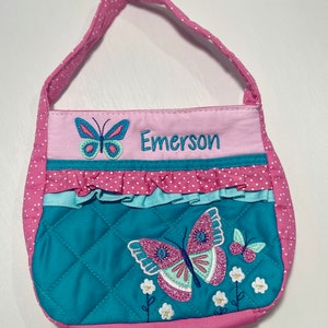 May include: A pink quilted tote bag with a blue butterfly design and the name "Emerson" embroidered on the front.