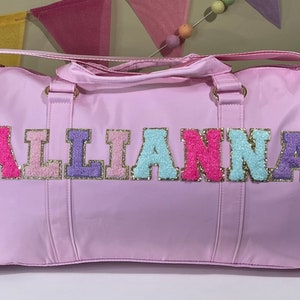 May include: A light pink duffel bag with the name "ALLIANNA" spelled out in colorful, sparkly letters.