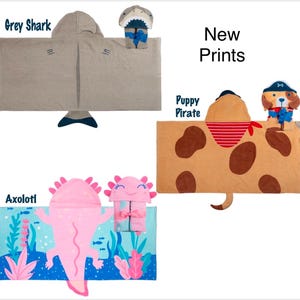 May include: Three hooded towels with different animal designs. The first towel is grey with a shark design, the second is brown with a puppy pirate design, and the third is blue with an axolotl design. New Prints.