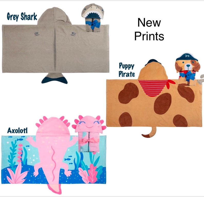 May include: Three hooded towels with different animal designs. The first towel is grey with a shark design, the second is brown with a puppy pirate design, and the third is blue with an axolotl design. New Prints.