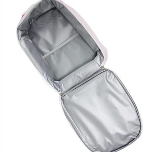 May include: Open, insulated lunch bag with a white and pink striped exterior. The interior features a silver lining, a mesh pocket, and a zippered closure. The bag is designed to keep food and drinks cool.