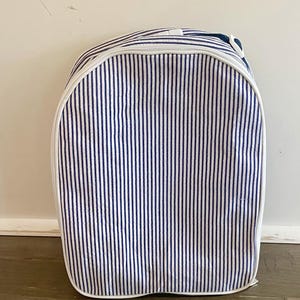 May include: A blue and white striped backpack with a white zipper and trim. The backpack has a rounded top and a handle. The vertical stripes are evenly spaced and cover the entire surface of the bag.