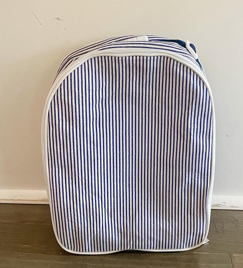 May include: A blue and white striped backpack with a white zipper and trim. The backpack has a rounded top and a handle. The vertical stripes are evenly spaced and cover the entire surface of the bag.