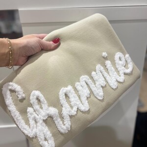 May include: A beige throw pillow with the word "Grammy" embroidered in white fluffy yarn.