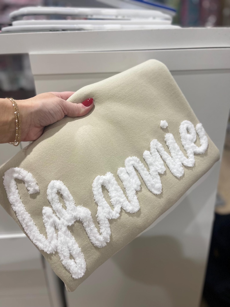 May include: A beige throw pillow with the word "Grammy" embroidered in white fluffy yarn.