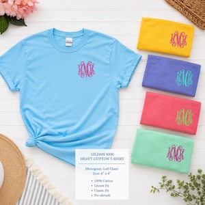 May include: A light blue Gildan 5000 heavy cotton t-shirt with a pink monogram on the left chest. The image also shows folded t-shirts in yellow, purple, coral, and mint green, each with a monogram. The text on the image says "Monogram: Left Chest Size: 4" x 4""