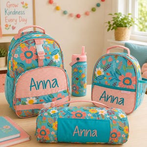 May include: A set of turquoise and pink floral-patterned backpacks, lunch bag, and water bottle. The backpack and lunch bag have the name "Anna" embroidered on them. The water bottle has a pink lid and straw.