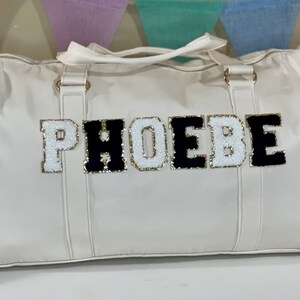 May include: White leather duffel bag with black and white felt letters spelling "PHOEBE".