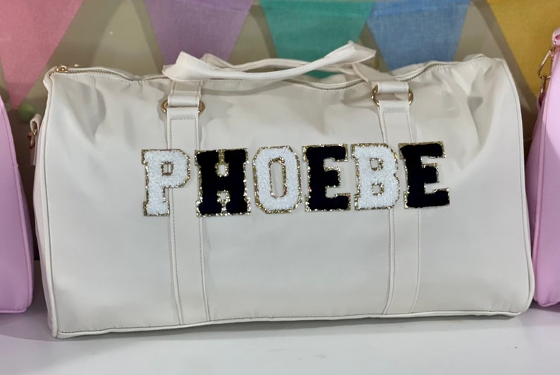 May include: White leather duffel bag with black and white felt letters spelling "PHOEBE".