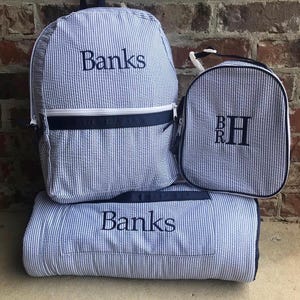 May include: A set of blue and white striped seersucker bags and a blanket. The backpack and blanket are embroidered with the name "Banks". The lunch bag has the initials "BRH".