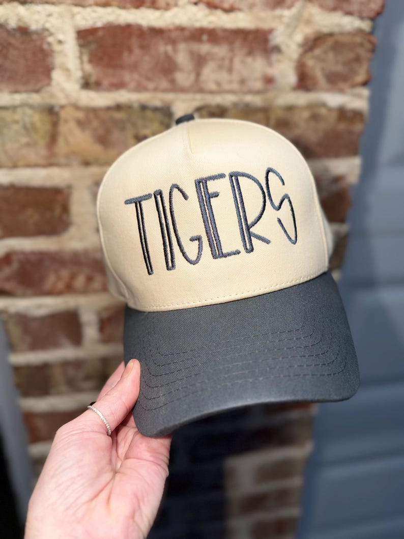 Op de afbeelding: Een beige en grijze baseballcap met het woord "TIGERS" in donkergrijs geborduurd. De cap heeft een gebogen klep en een gestructureerd ontwerp, voor sportfans.
