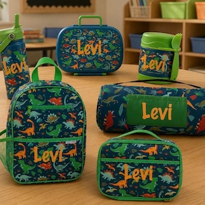 May include: A collection of children's school supplies featuring a dinosaur theme. Includes a backpack, lunch bag, water bottle, food container, and a cylindrical mat. Each item is navy blue with a green trim and dinosaur illustrations, and the name "Levi" in orange.