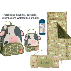 May include: A farm-themed set including a backpack, lunchbox, water bottle, and nap mat. The backpack and lunchbox feature a cow design. The nap mat and blanket have a farm scene print. The water bottle is blue with a cow illustration. The name "Levi" is printed on the items.