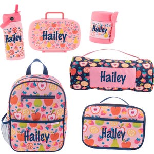 May include: A collection of pink and blue school supplies featuring a fruit pattern. Includes a water bottle, lunchbox, food container, backpack, and a picnic blanket, all personalized with the name "Hailey".