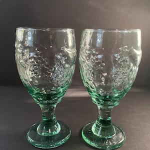 May include: Two green glass goblets with a textured, bubbled design. The goblets have a round base and a stem.