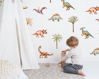 Puede incluir: Un niño juega con bloques de madera frente a una pared blanca con calcomanías de dinosaurios y palmeras. Las calcomanías son de varios colores, incluyendo verde, marrón, naranja y azul.