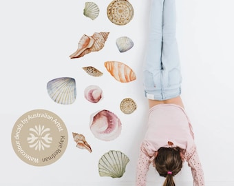 May include: Watercolor decals of various seashells in shades of brown, pink, and green, arranged on a white wall. The decals are designed by Australian Artist Kaye Redman. A child is doing a handstand near the wall.