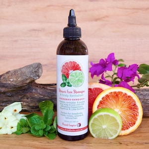 May include: A brown glass bottle of "Shaver Free Shampoo & Scalp Revitaliser" with a white label featuring a grapefruit, lime, and mint illustration. The bottle is sitting on a wooden surface with a grapefruit, lime, and flowers.