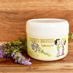 Pode incluir: Um frasco branco de gel de endurecimento Dread Empire com um rótulo amarelo com um casal de desenhos animados e raminhos de lavanda. O gel contém aloe vera, alecrim e óleos essenciais de lavanda. Um raminho de lavanda está ao lado do frasco.