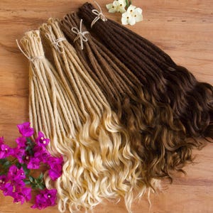 May include: A set of synthetic dreadlocks in three shades of brown, blonde, and light blonde. The dreadlocks are arranged in a fan shape on a wooden surface.