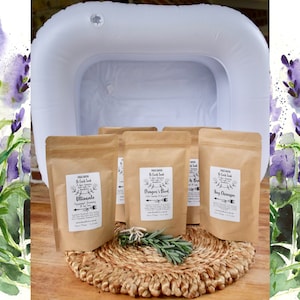 Op de afbeelding: Vier bruine papieren zakjes met etiketten waarop "Ultimate", "Dragon's Blood", "Honey Champagne" en "Lavender & Eucalyptus" staat. De zakjes liggen op een geweven strooien mat. Op de achtergrond is een wit opblaasbaar voetbad te zien.