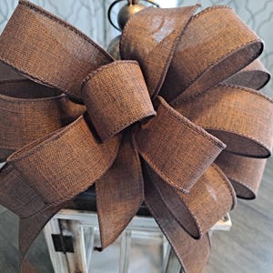 May include: A large brown burlap bow with a wired edge. The bow is tied around a lantern.