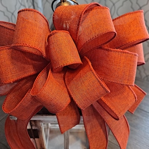 May include: A large, orange, burlap bow with a wired edge. The bow is tied in a decorative knot and has a rustic, farmhouse style.