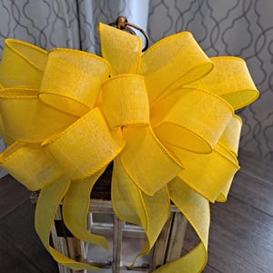May include: A large, bright yellow bow made from wired ribbon. The bow is tied around a lantern.