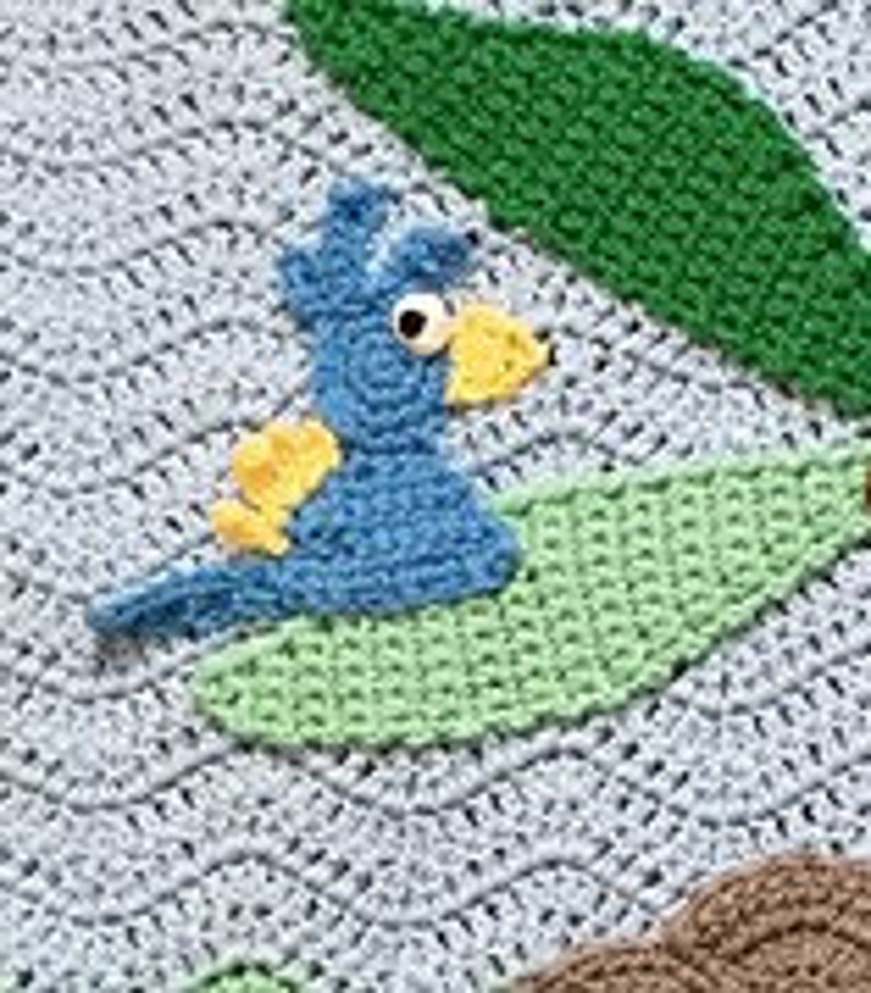 May include: A blue bird with yellow accents is crocheted and sitting on a green leaf. The bird has large black eyes and a small yellow beak. The leaf is crocheted and has a light green color.