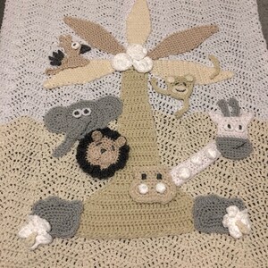 May include: A crocheted baby blanket with a jungle theme. The blanket features a palm tree, an elephant, a lion, a giraffe, and a monkey. The blanket is made in beige, brown, and gray yarn.