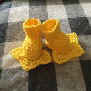 Puede incluir: Un par de botitas de bebé de crochet amarillo con suelas en forma de estrella.