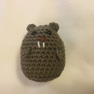 May include: A handmade, brown crocheted beaver toy with black eyes, a brown nose, and two white tusks. The plush toy has small, rounded ears and a rounded body. The beaver is made of a textured yarn.