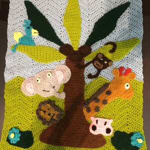May include: A crocheted baby blanket with a green jungle theme. The blanket features a brown tree with green leaves, a yellow bird, a brown monkey, a pink pig, a brown elephant, and an orange giraffe.