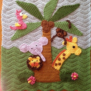 May include: A crocheted baby blanket with a jungle theme. The blanket features a palm tree with a pink bird, a purple elephant, a yellow giraffe, and a brown monkey hanging from the tree. The blanket is green and brown with pink and yellow flowers.