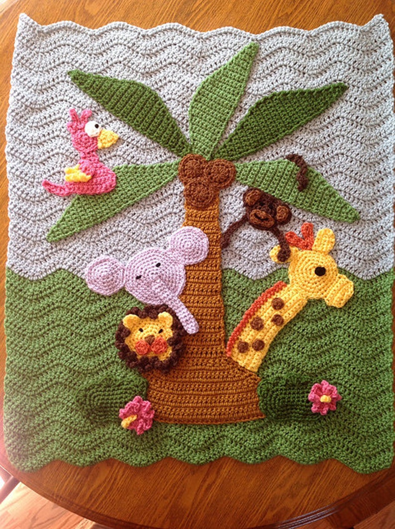 May include: A crocheted baby blanket with a jungle theme. The blanket features a palm tree with a pink bird, a purple elephant, a yellow giraffe, and a brown monkey hanging from the tree. The blanket is green and brown with pink and yellow flowers.