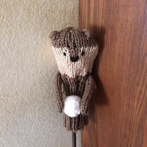 Könnte beinhalten: Gestrickte braune und beigefarbene Golfkopf-Hülle in Form eines Otters, der einen weißen Golfball hält.