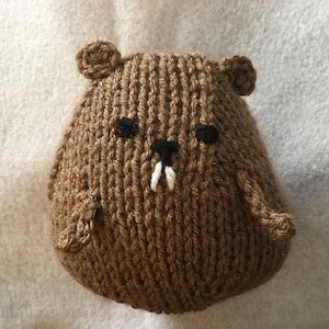 May include: A brown knitted beaver toy with black eyes and a white tooth. The handmade plush animal has small ears and arms. The beaver is made of a soft, textured yarn.