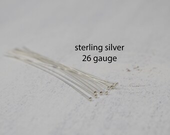 May include: A collection of thin, silver-colored metal wires, likely for jewelry making, are arranged on a light-colored surface. The text "sterling silver 26 gauge" is visible, indicating the material and wire thickness.
